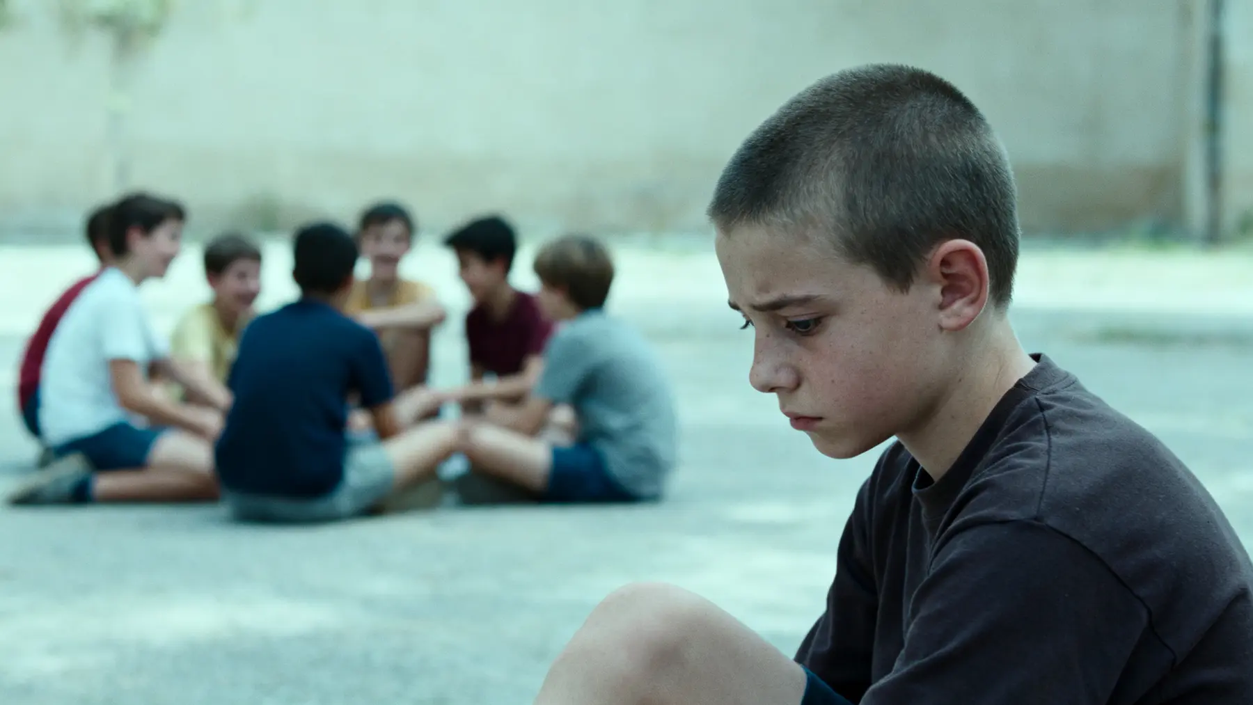 Downcast boy sitting apart from a group of other boys laughing behind him