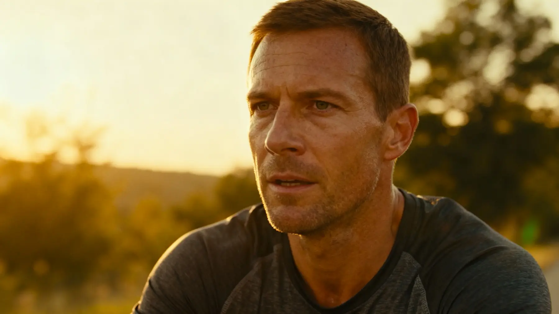 Weary man in a gray shirt outdoors at golden hour, tired and downcast