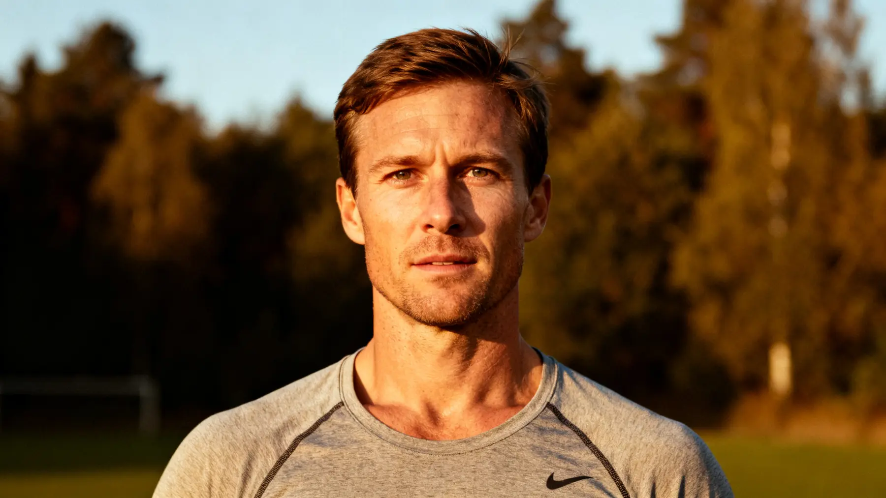 Lean athletic man in a gray shirt standing on a field at sunset