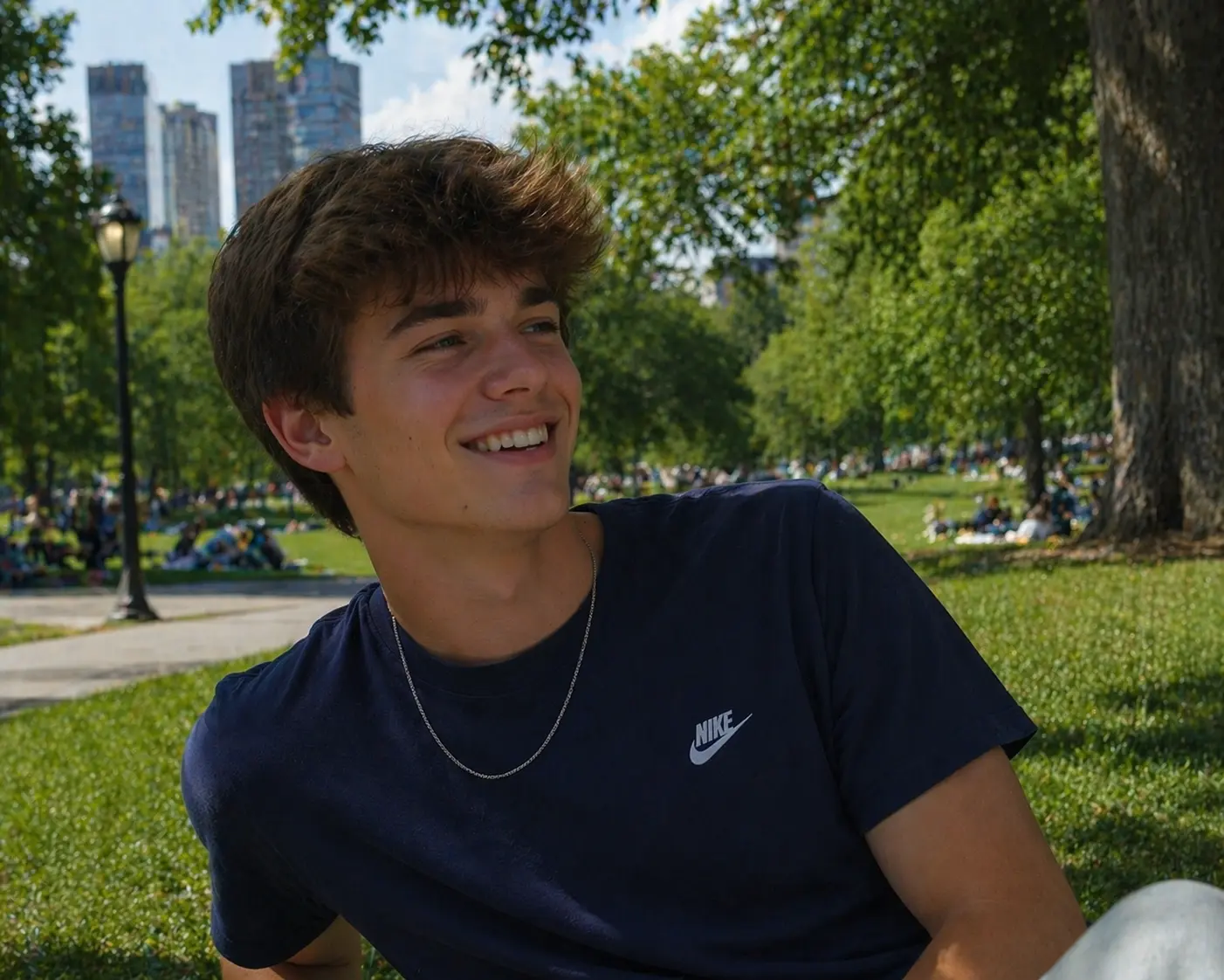 Smiling young man in a navy tee sitting on grass in a sunny city park