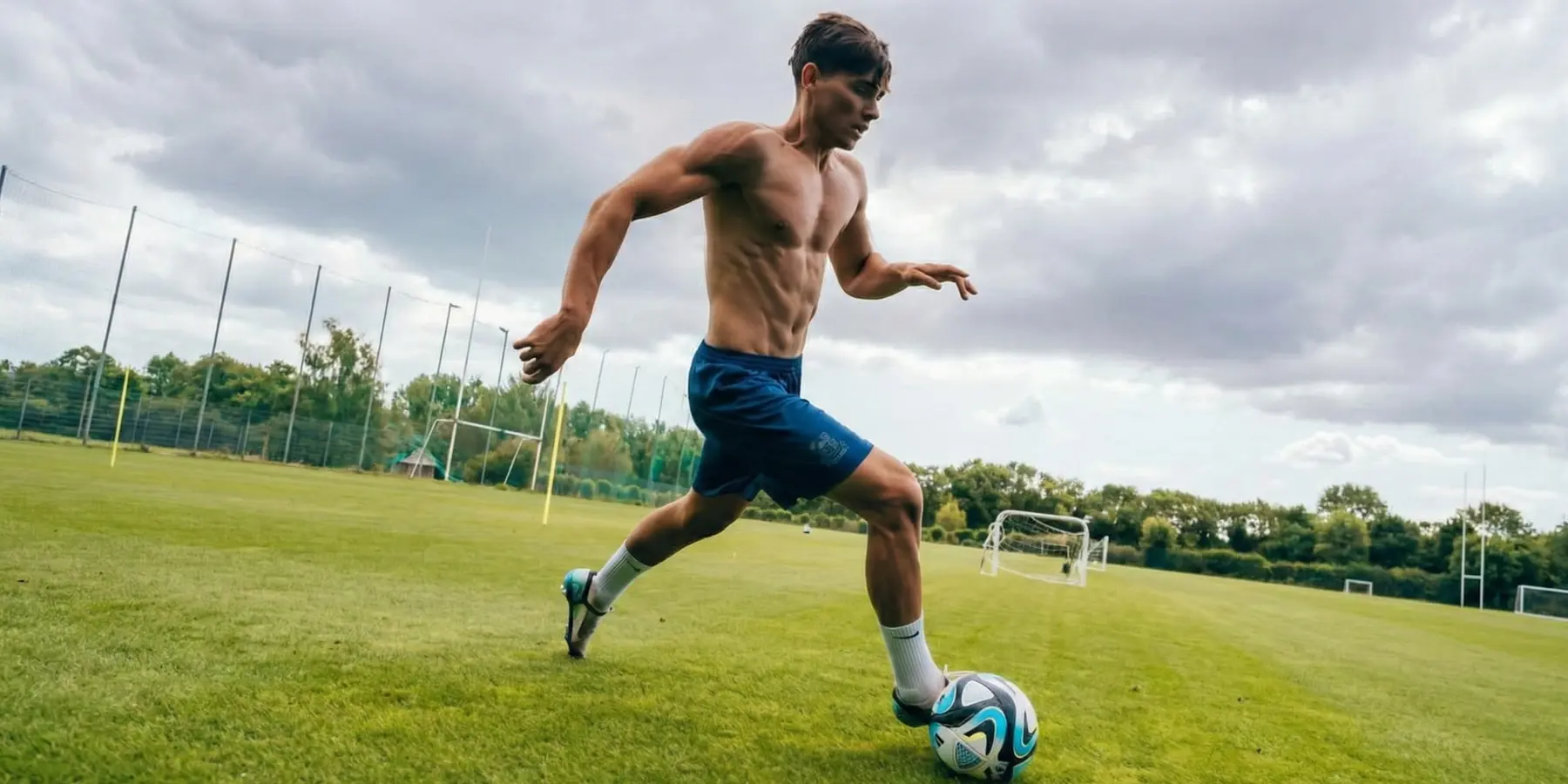 Shirtless young man dribbling a soccer ball across a green field