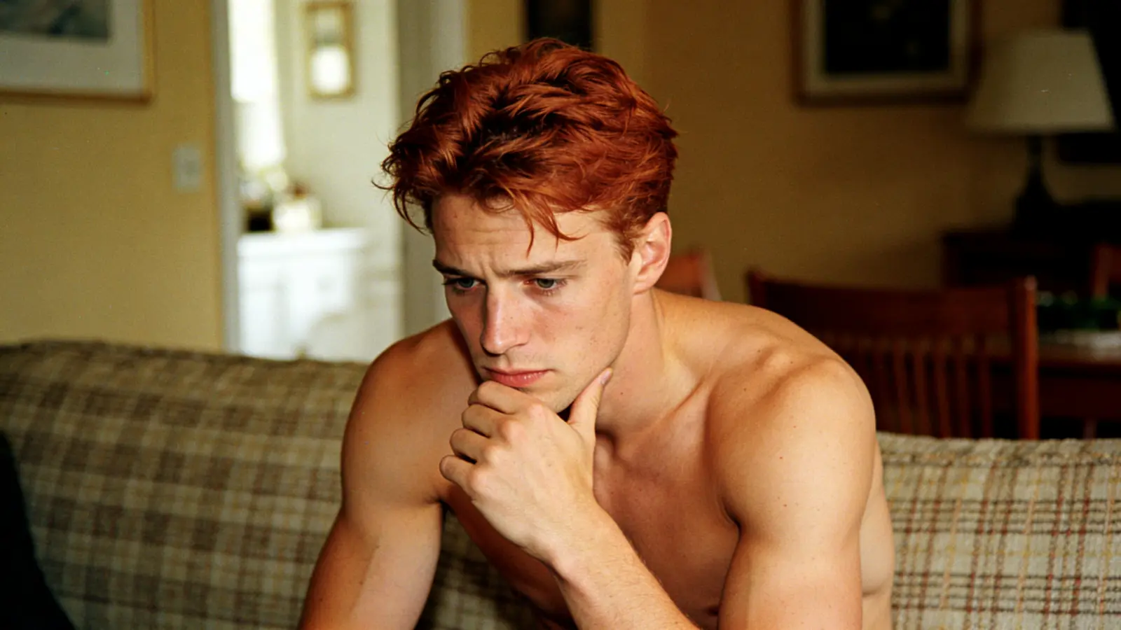Young man on a couch looking quietly worried and lost in thought