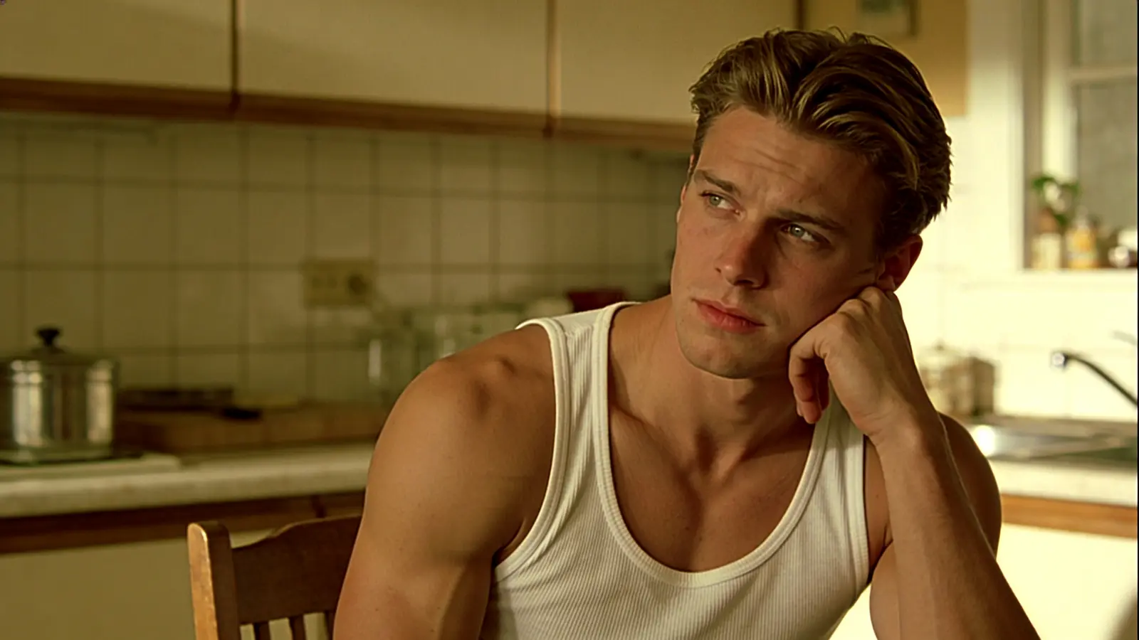 A young man sits at a kitchen table thinking something through with an uncertain expression