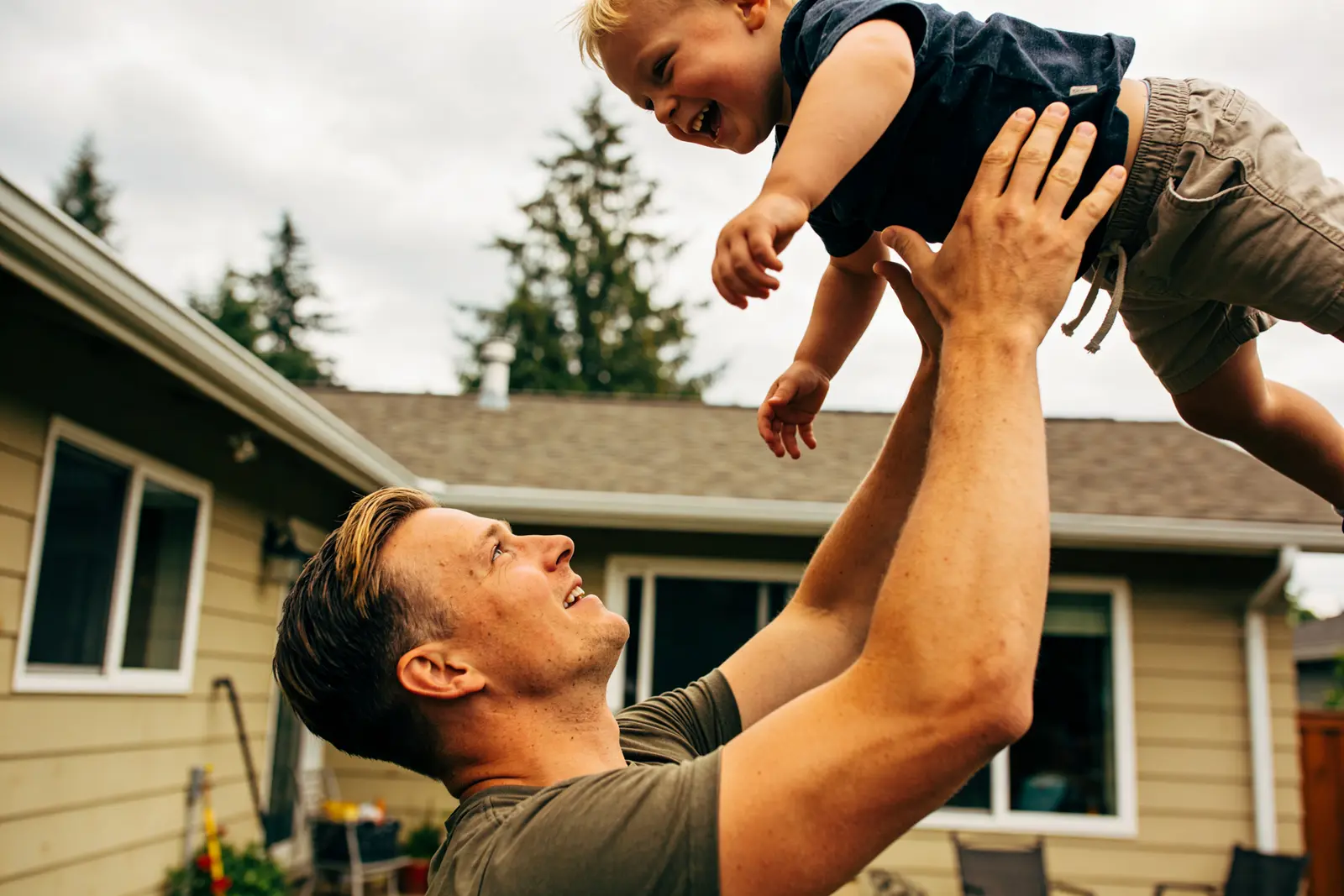 Smiling father lifting his laughing toddler overhead in a suburban backyard