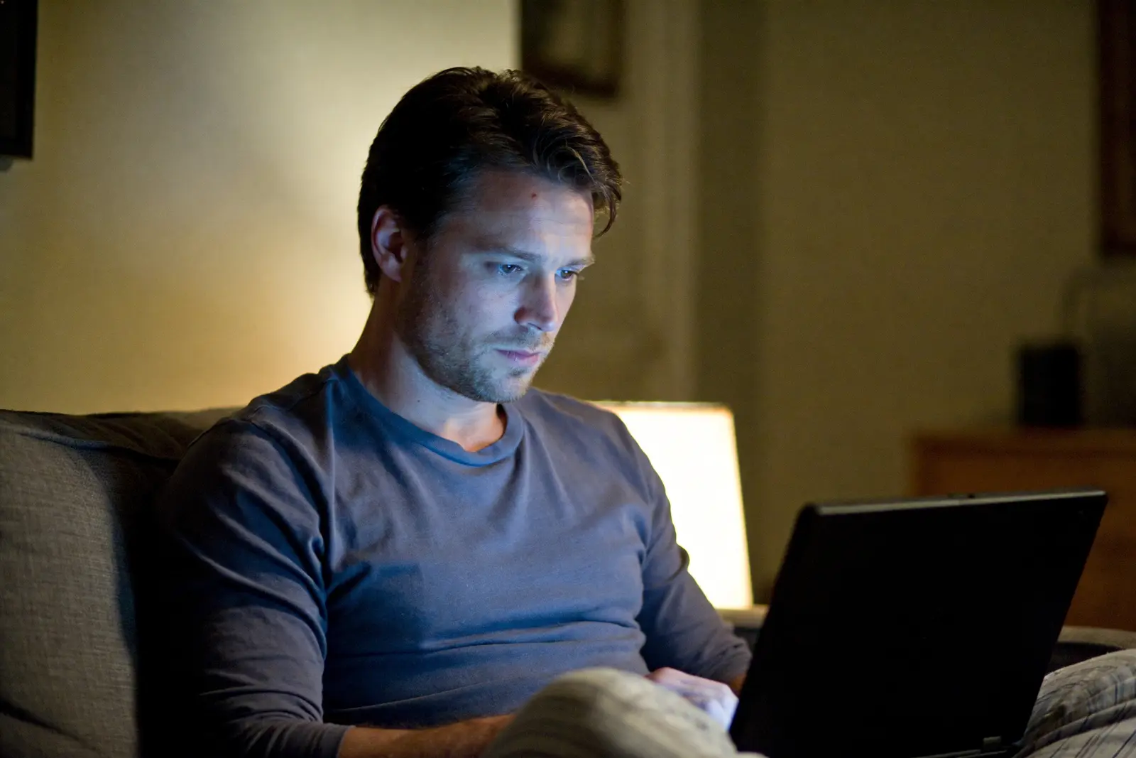 Man on a couch at night, face lit by a laptop screen in a dim living room