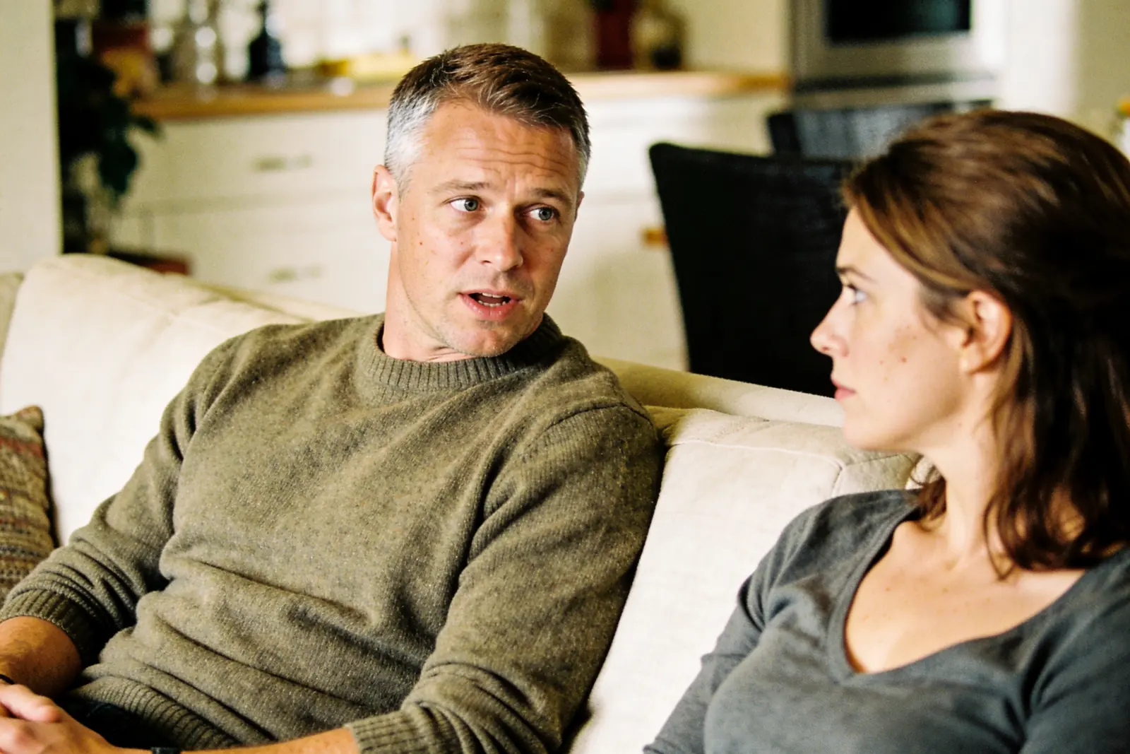 Man on a couch talking earnestly with a woman who listens beside him
