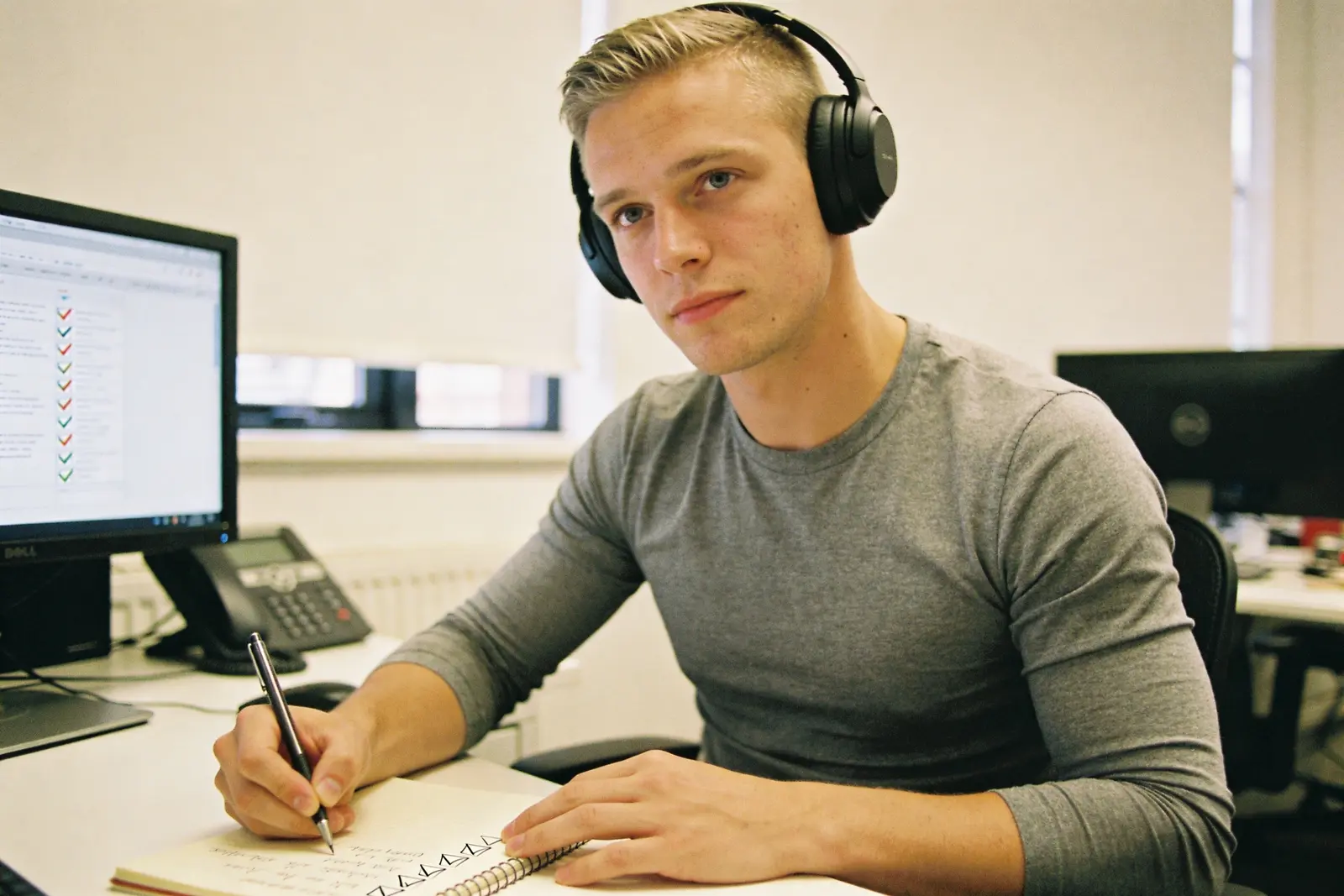 Focused young man wearing headphones taking notes at an office desk