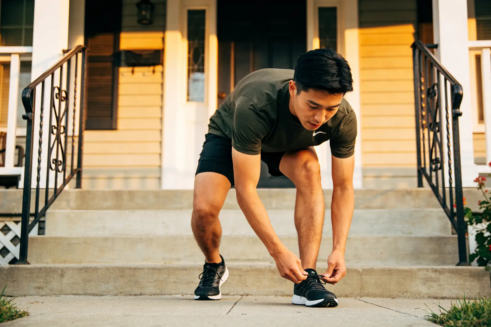 Runner tying his shoe on the front steps of a house at sunset