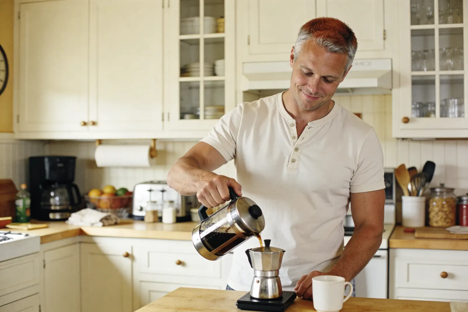 Smiling man pouring fresh coffee from a French press in a bright kitchen