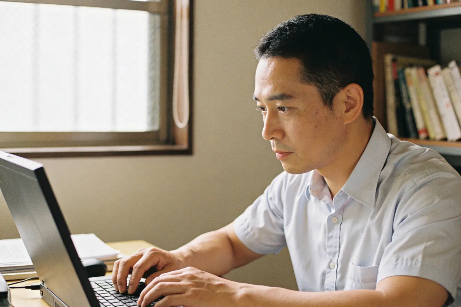 Focused man typing at a laptop in a home study lined with books
