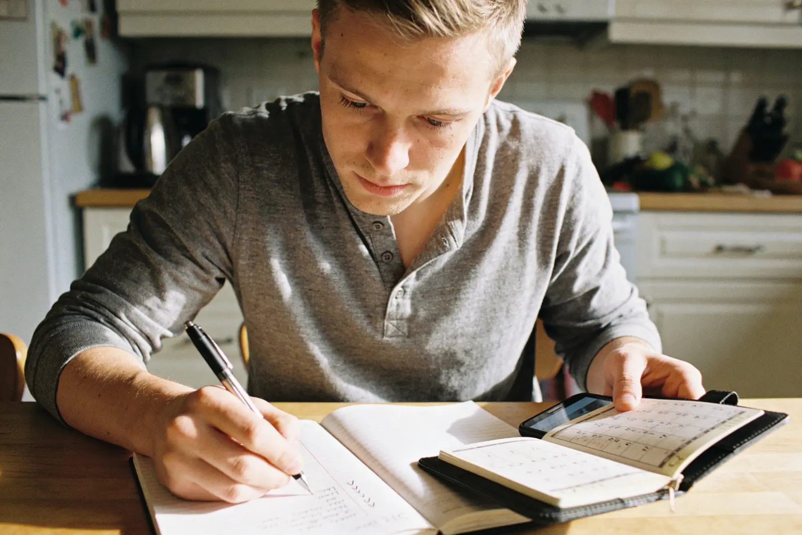 Young man writing in a planner beside a calendar and phone at a table