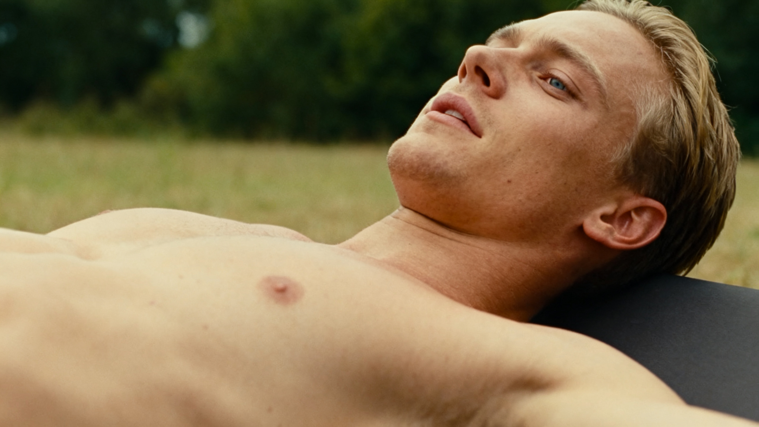 Relaxed shirtless man lying back outdoors with his face tilted toward the sky