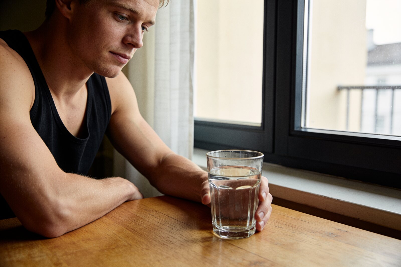Fit man at a wood table with a glass of water, morning light, relaxed