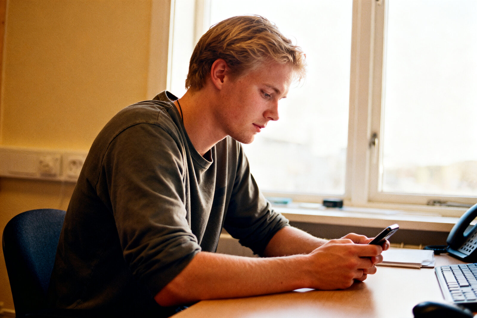 Man in casual clothes at a desk looking at his phone, calm and focused, natural light