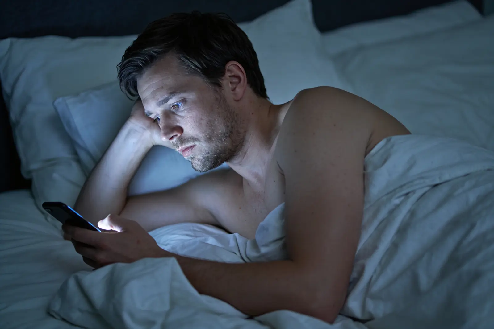 Tired man checking the time on his phone in the dark, hours into a sleepless night