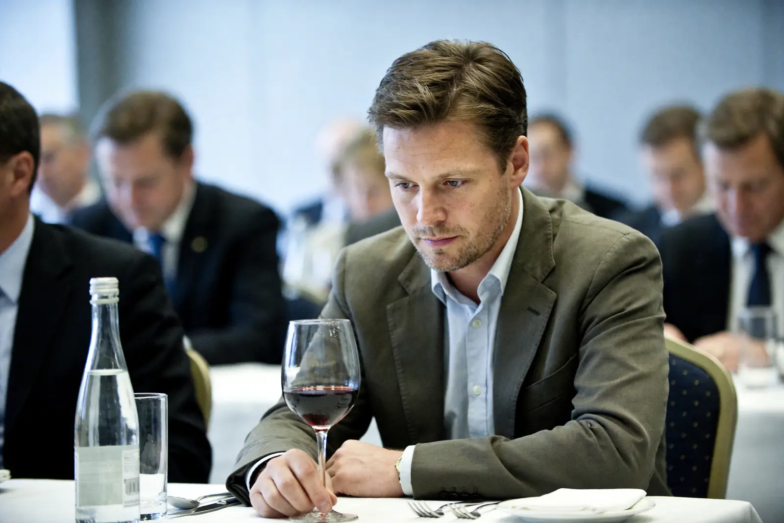 Man at a social event hesitating with a glass of wine on the table in front of him