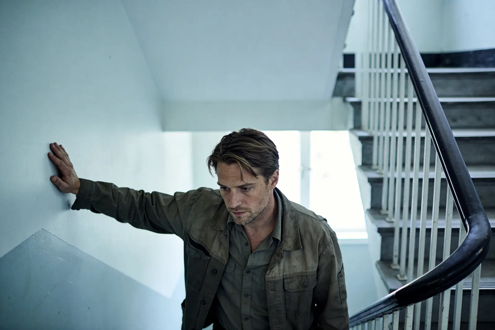 A man stopped on a stair landing, hand on the rail, in a moment of realization