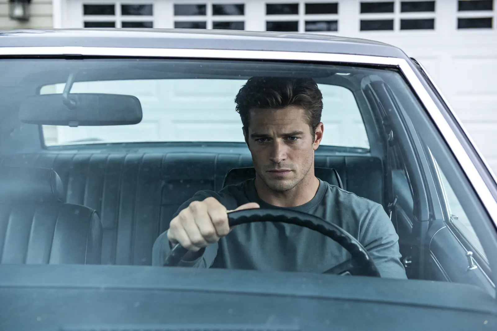 A handsome man pausing alone in his parked car in the driveway, catching a quiet realization