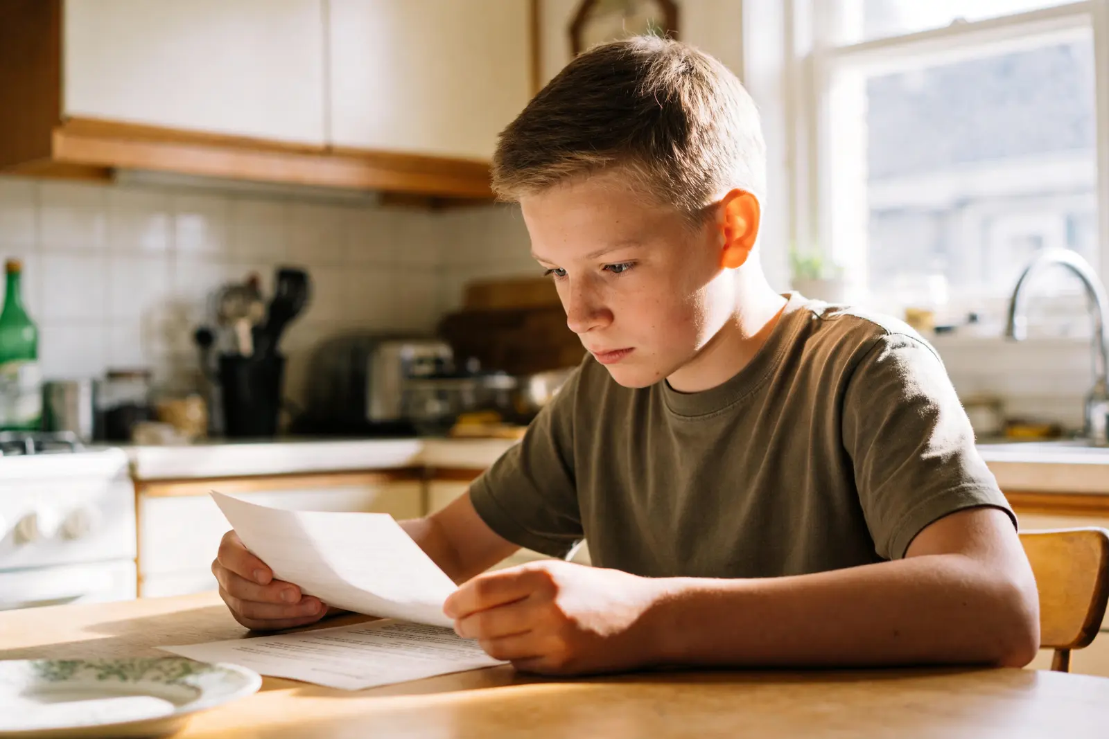 Calm teenage boy reading at the kitchen table in the morning