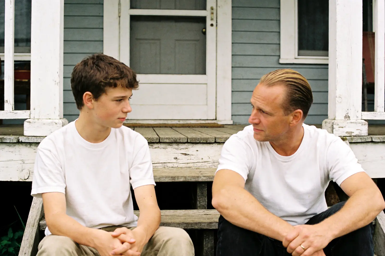 Father sitting quietly beside his teenage son on the porch steps