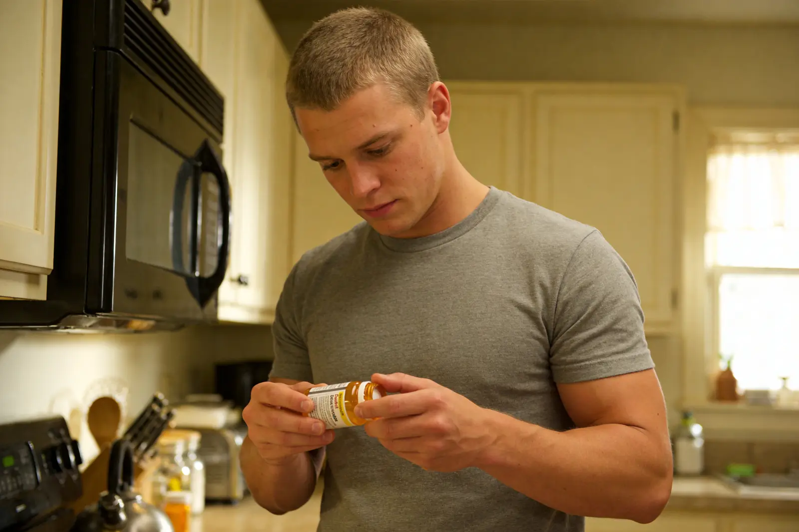 Man reading a medication label at a kitchen counter in calm morning light