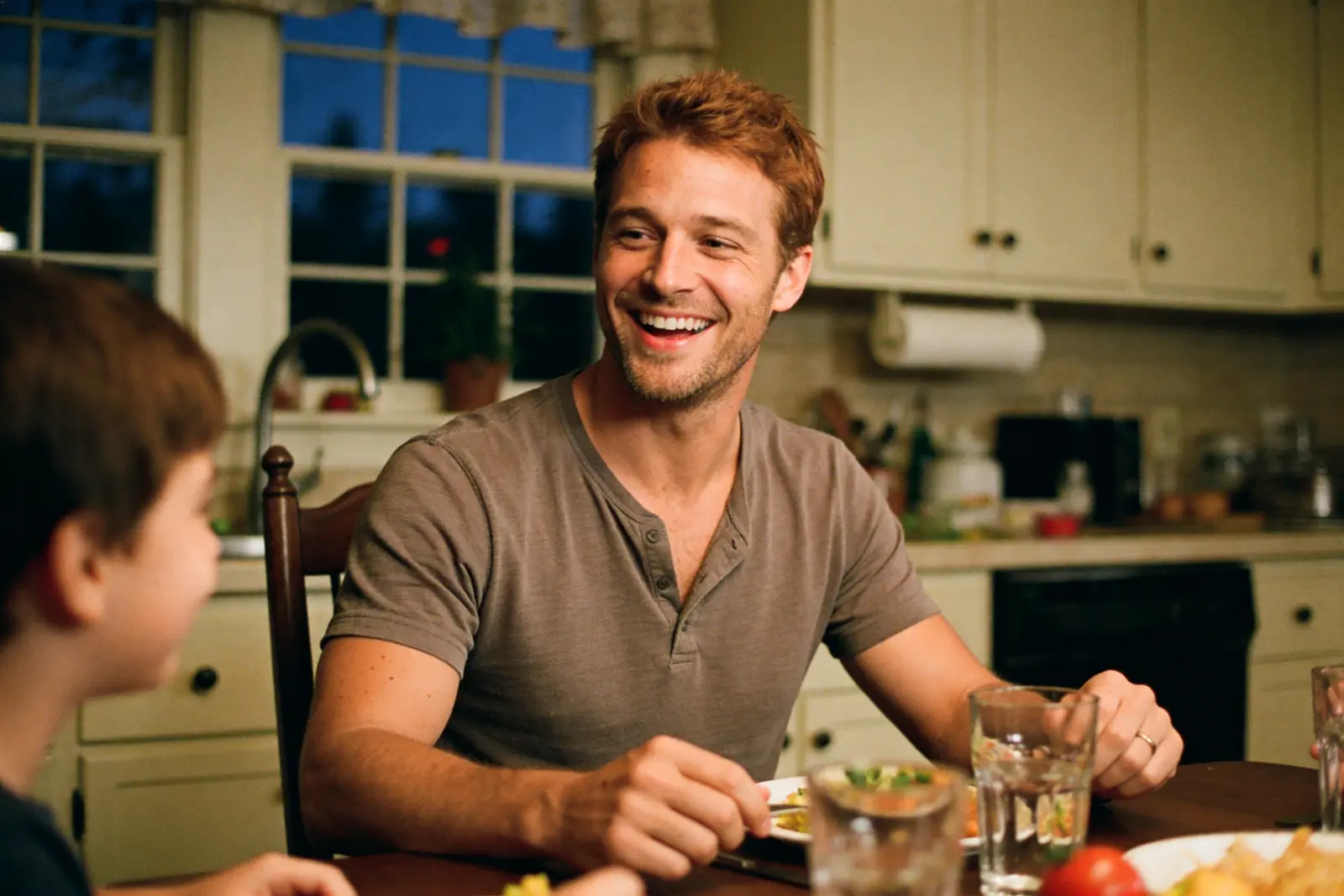A father in his late thirties relaxed at the dinner table with his kids in the evening