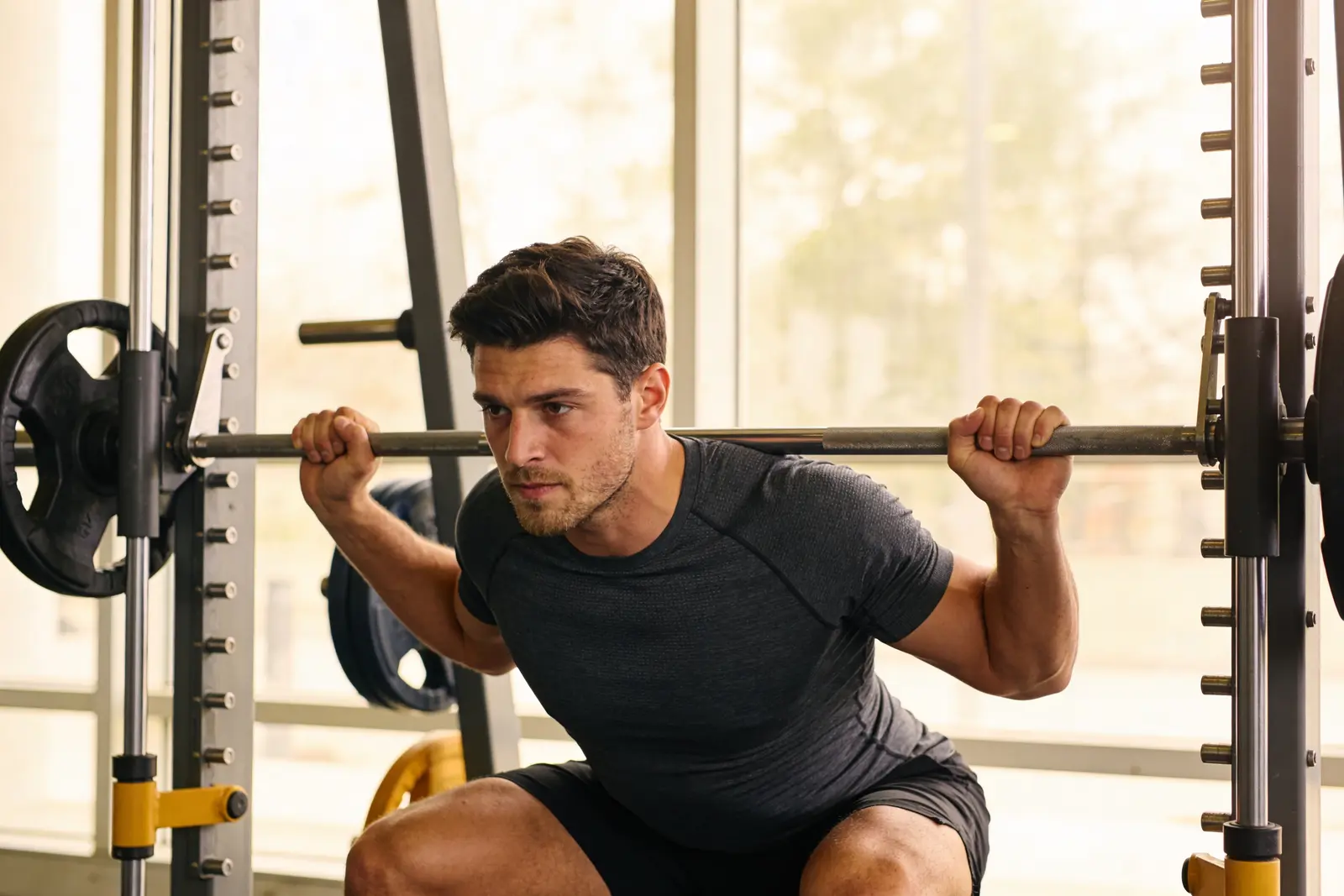 A fit young man mid-squat at the rack in a bright gym