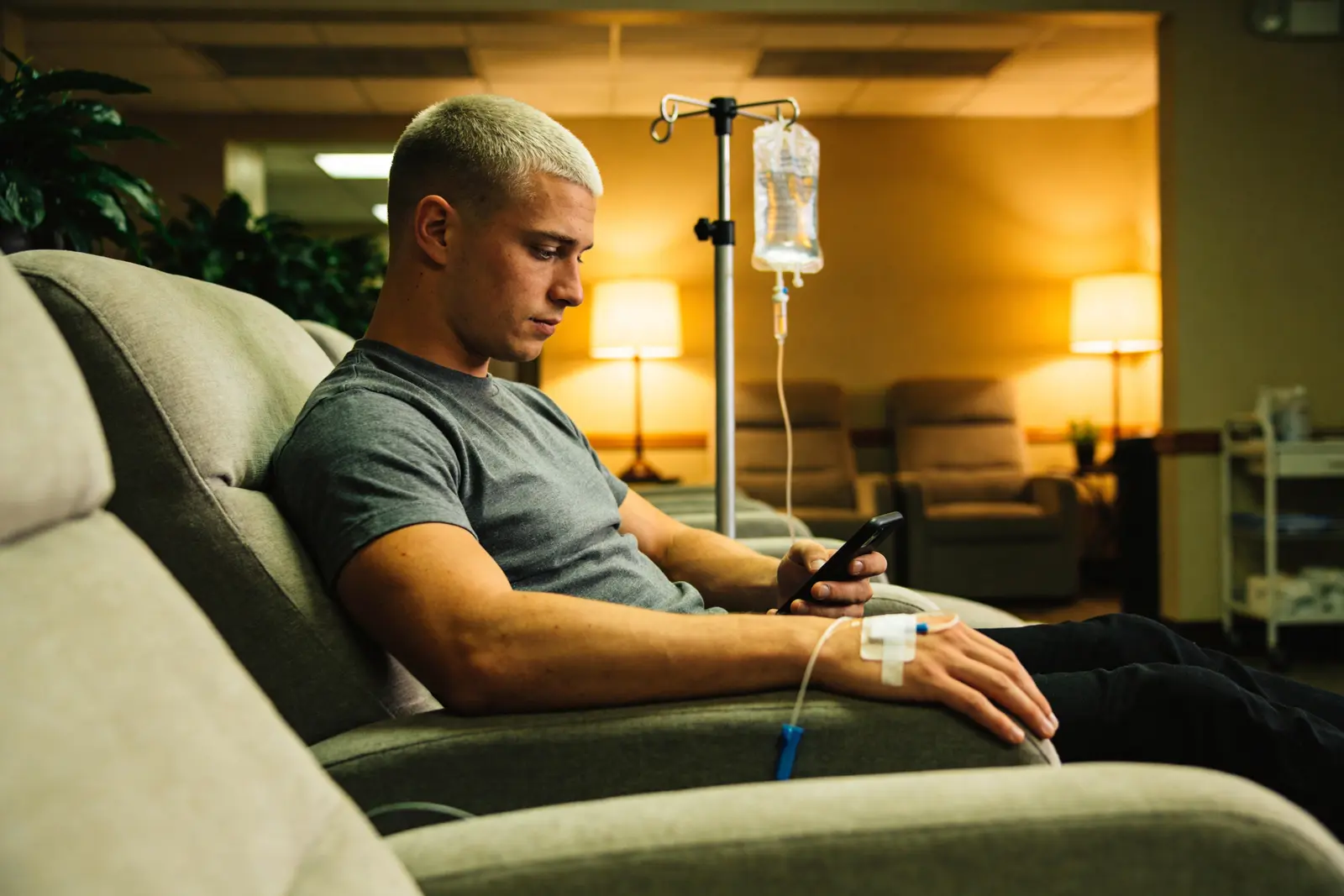 Man in a wellness-clinic recliner mid-IV drip, looking at his phone