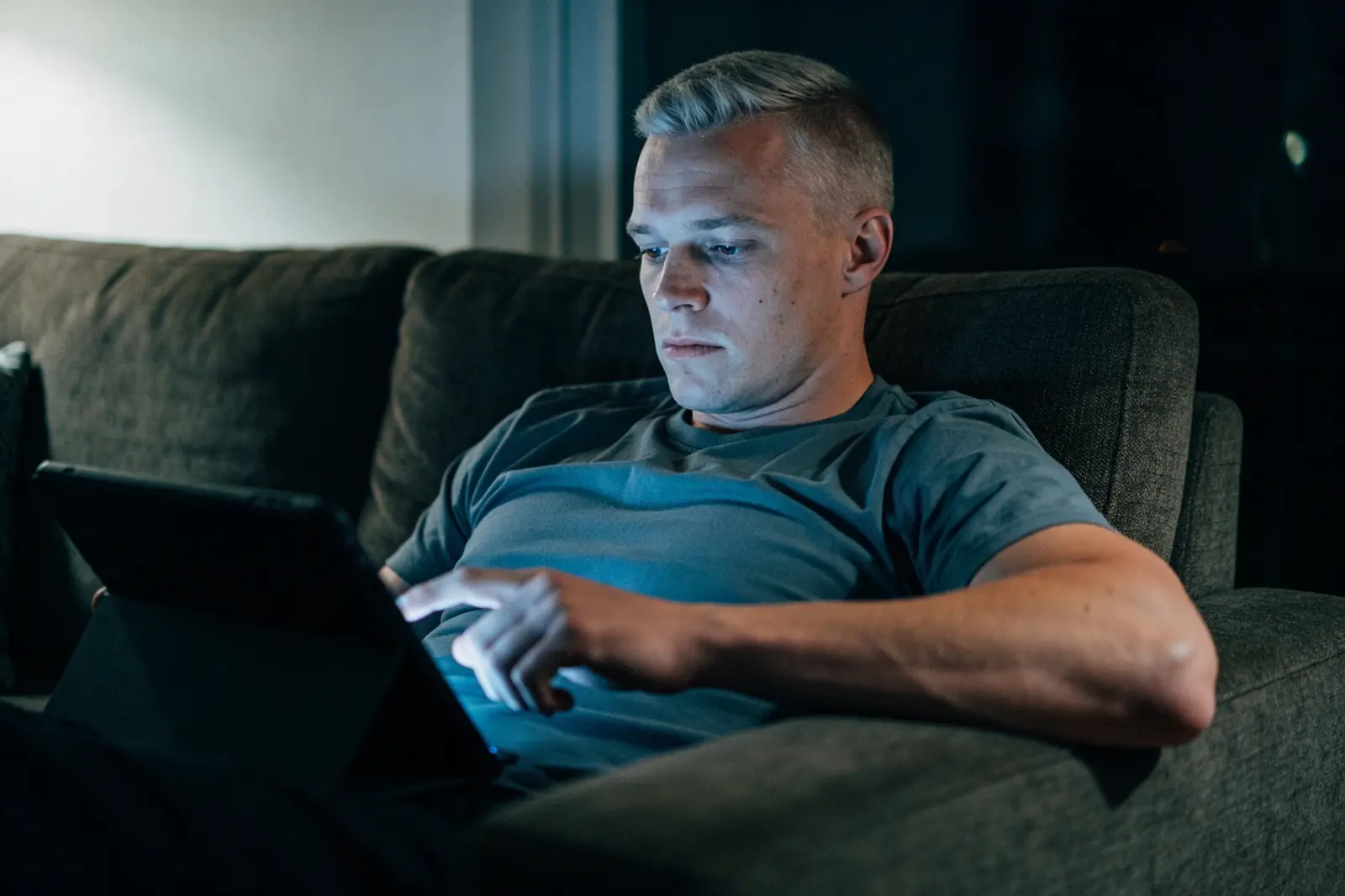 A young man up late on the couch still working on a tablet instead of sleeping